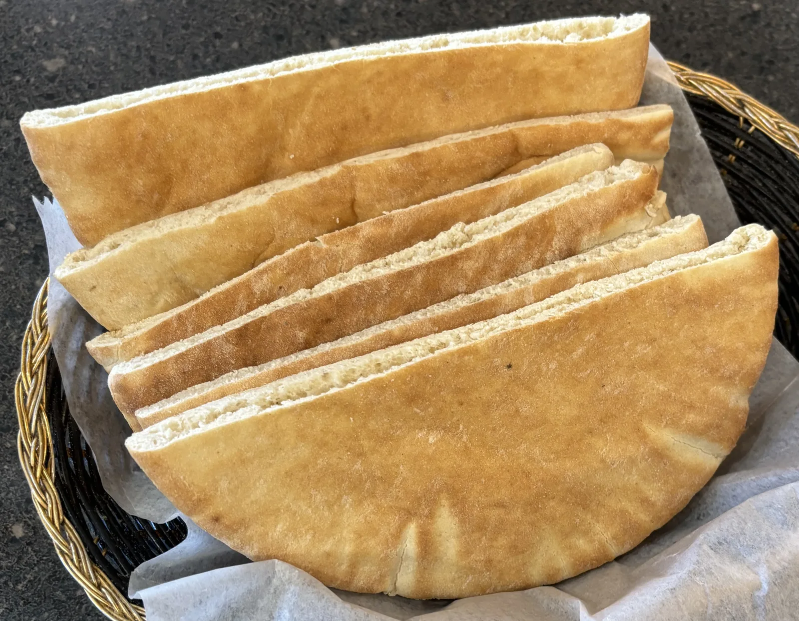 Wooden basket with several pieces of homemade pita bread on wooden table. Copy space.